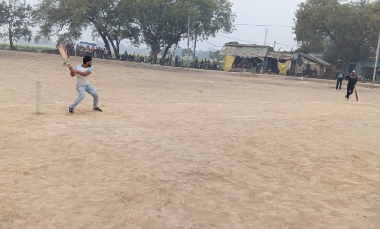 क्रिकेट मैदान पर शॉट खेलता बल्लेबाज और फील्डिंग करती टीम।